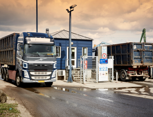 To lastbiler med blå 83 containere på køre ind og ud af vejeanlæg med skrot til genbrug