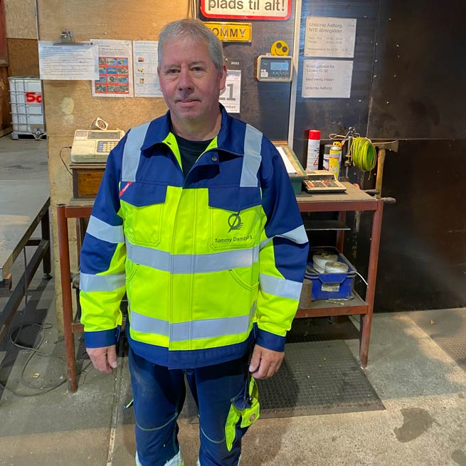 Tommy Damborg, skrotspecialist, stående i gult arbejdstøj foran opslagstavle Tommy Damborg, skrotspecialist, stående i gult arbejdstøj foran opslagstavle
