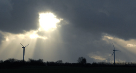 vindmøller-på-mark Vindmøller på en mark med mørk himmel og solen skinner igennem nogle mørke skyer.